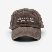 A brown denim cap with the text 'CATS & WINE MAKE EVERYTHING FINE' embroidered on the front.