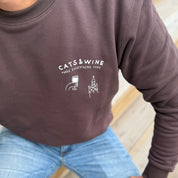 Person wearing a brown sweatshirt with 'Cats & Wine Make Everything Fine' text and graphics.